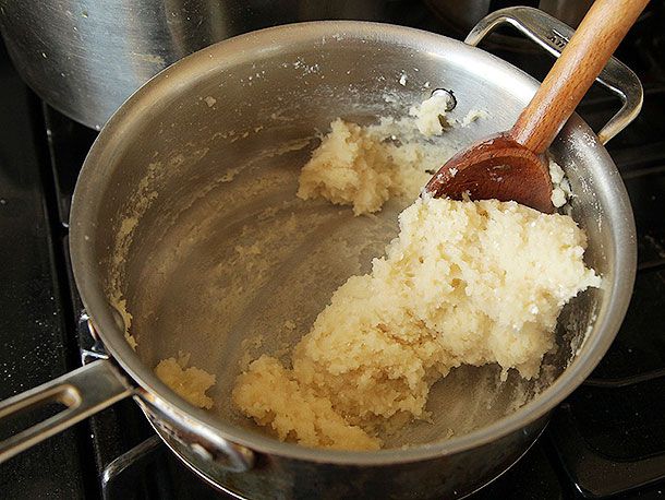 Mixture for pate a choux is being cooked and vigorously stirred with a wooden spoon.