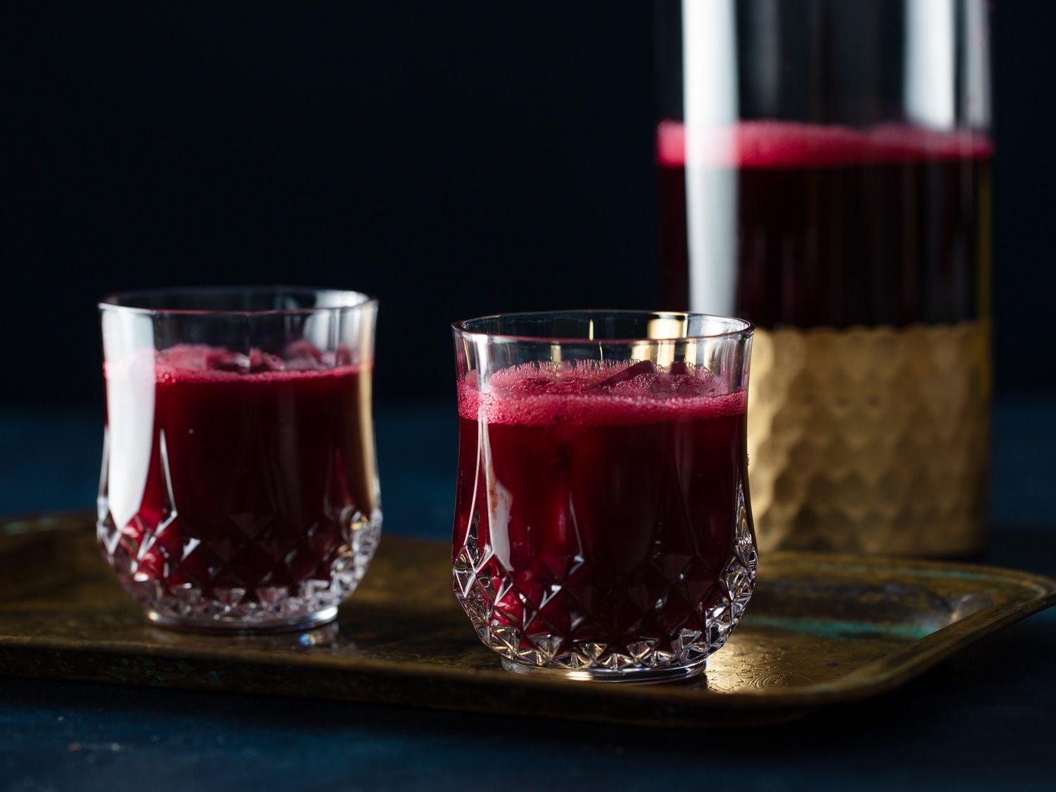 Two glasses of Jamaican sorrel (hibiscus) resting on a platter with a pitcher of the drink in the background.