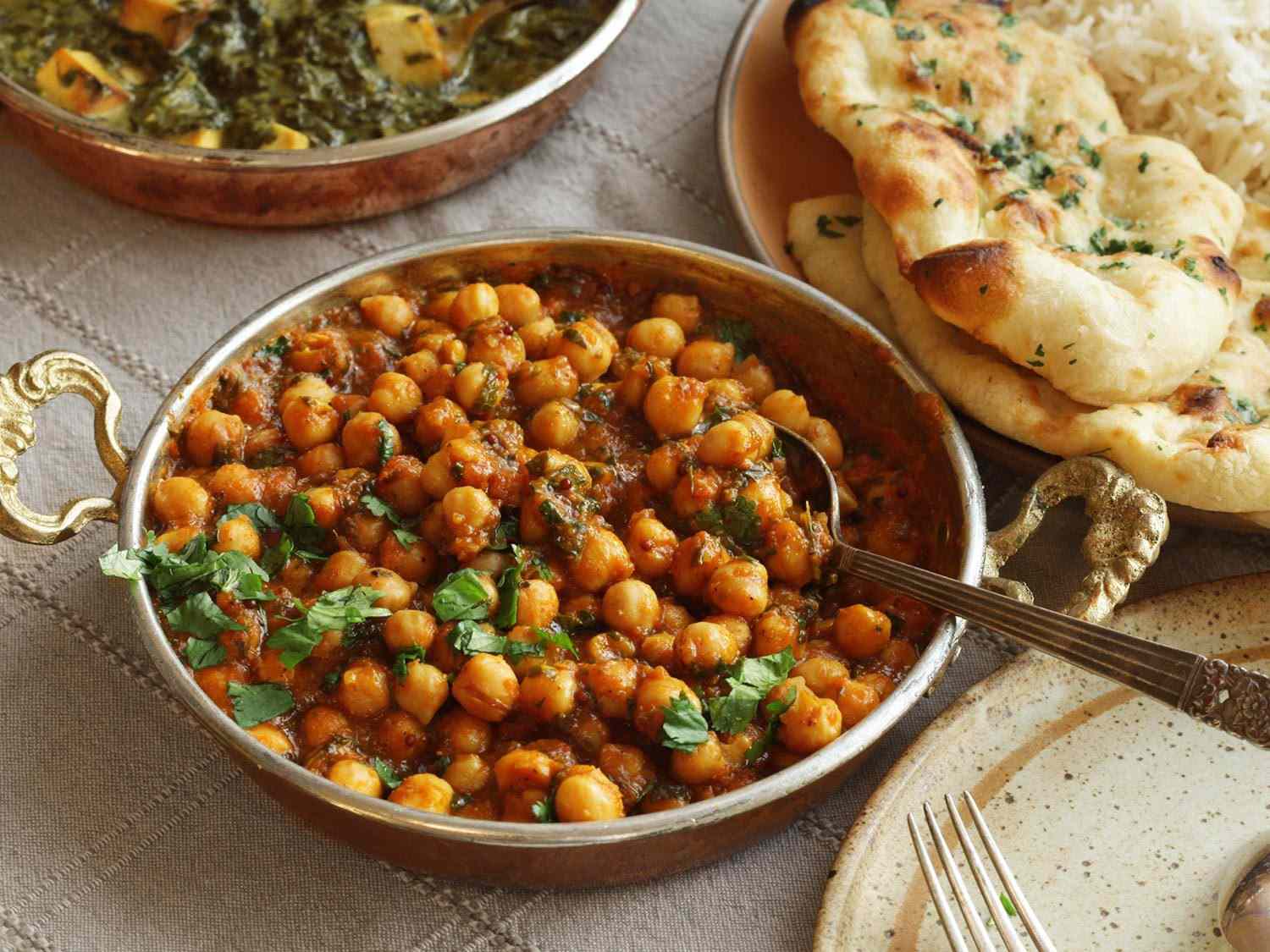 Channa masala in a serving bowl, next to a plate of naan. 