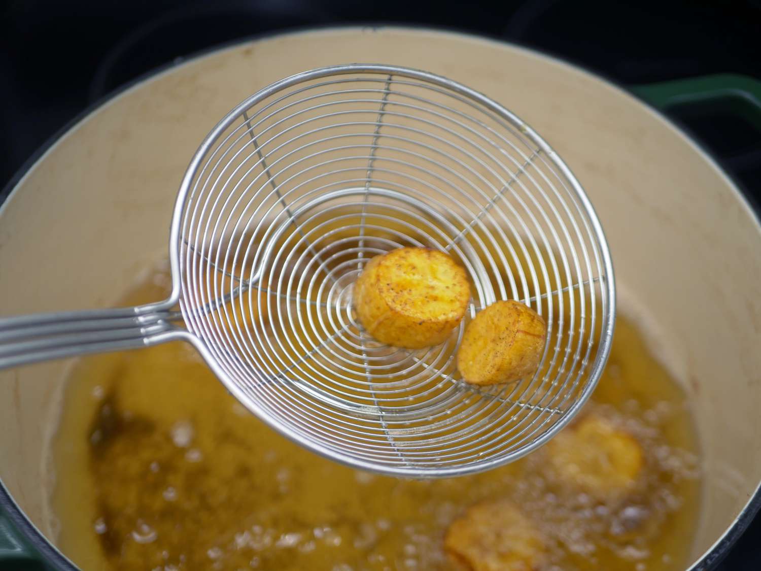 closeup image of the basket of a spider strainer holding fried plantain pieces over a Dutch oven
