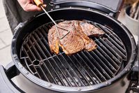 A person cooks meat in the Broil King Keg Kamado Charcoal Grill