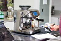 Breville Barista Touch Impress Espresso Machine with Grinder on a table, brewing a shot of espresso