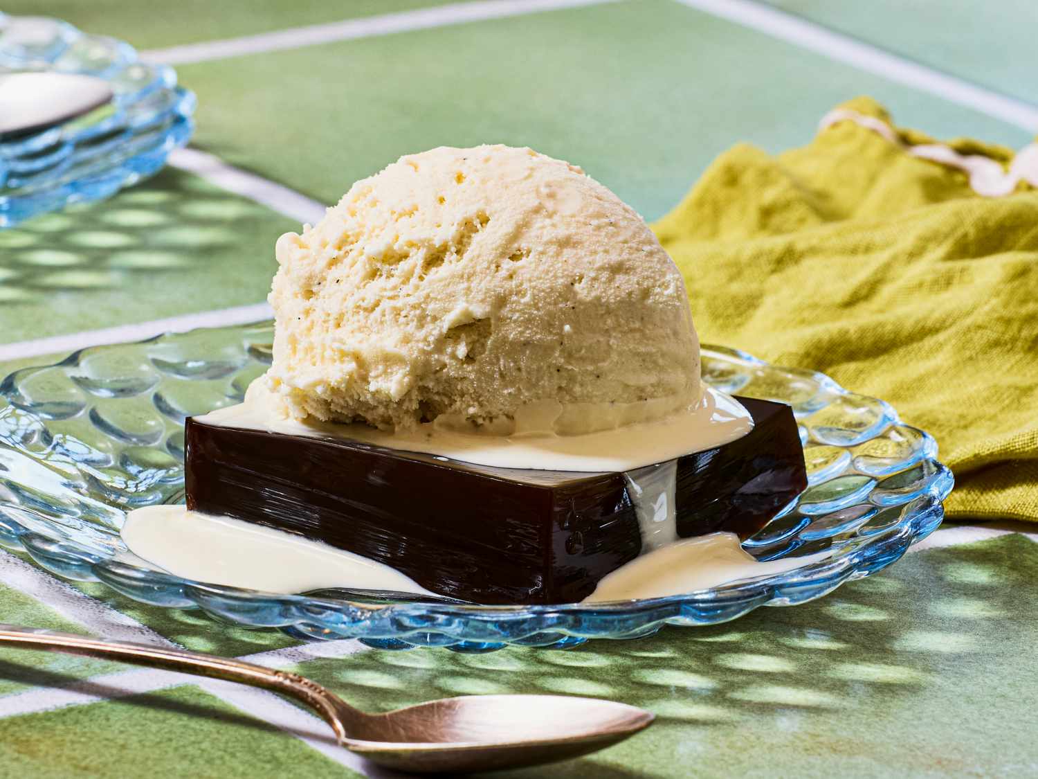 A dessert featuring a block of coffeeflavored gelatin topped with a scoop of ice cream and drizzled with cream on a glass plate