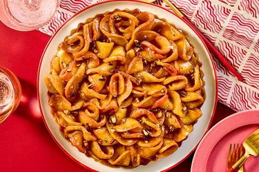 A caramel apple tart with decorative crust garnished with nuts placed on a red table setting