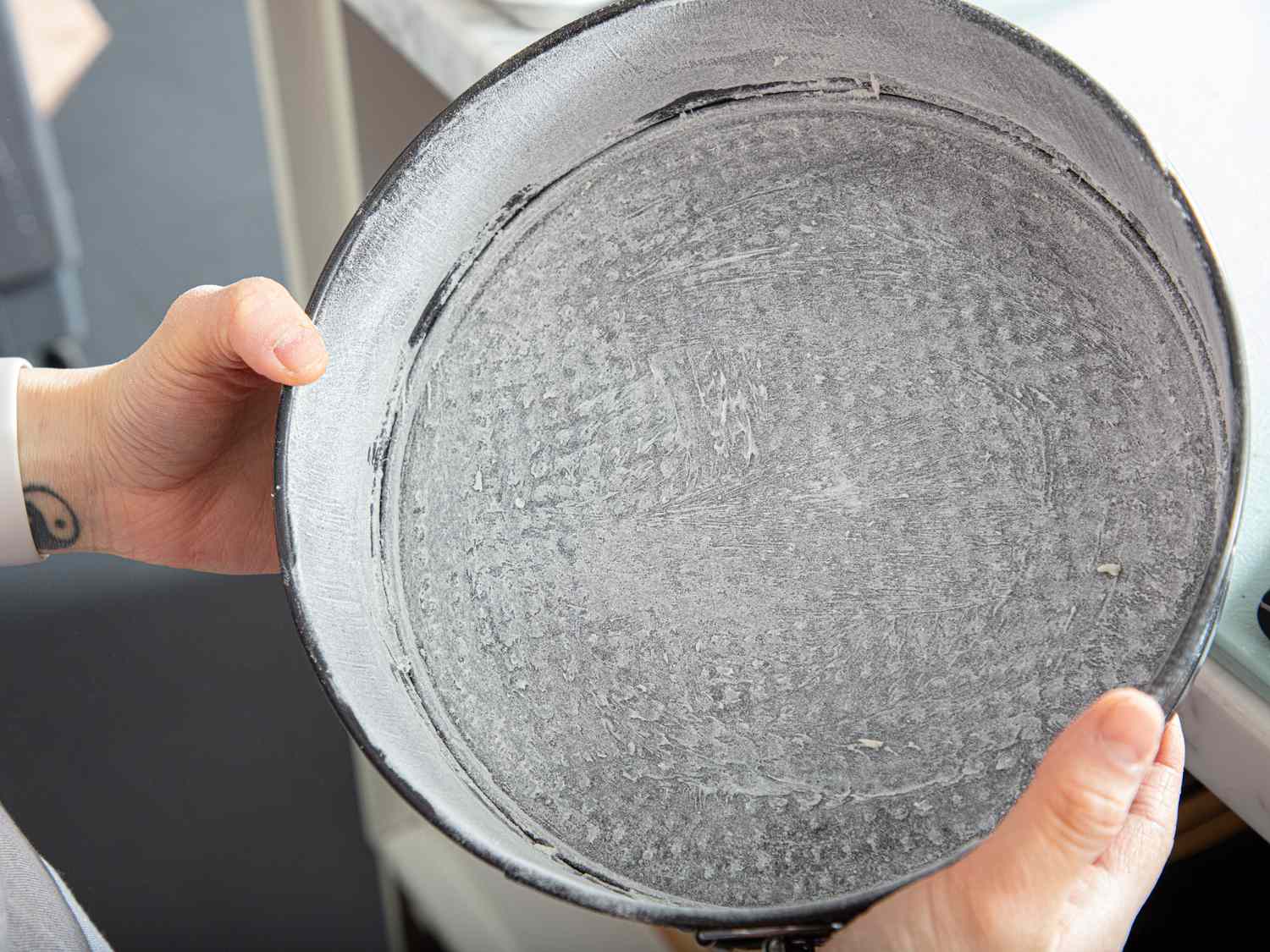 Hands holding a round baking pan prepared for making cheesecake