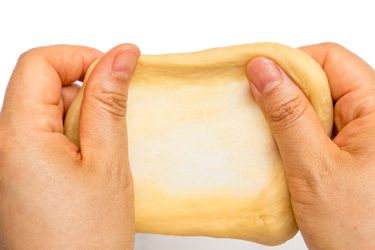 Hands holding up dough, checking the consistency using the window pan test 