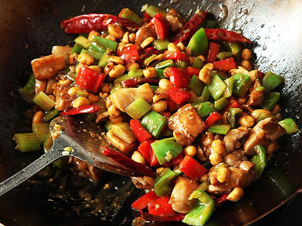 Adding sauce and chicken to stir-fried peppers, celery, and peanuts in a wok for takeout-style kung pao chicken.