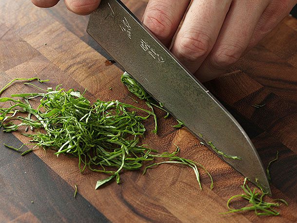 A knife about to be pulled backwards through some rolled up herbs.
