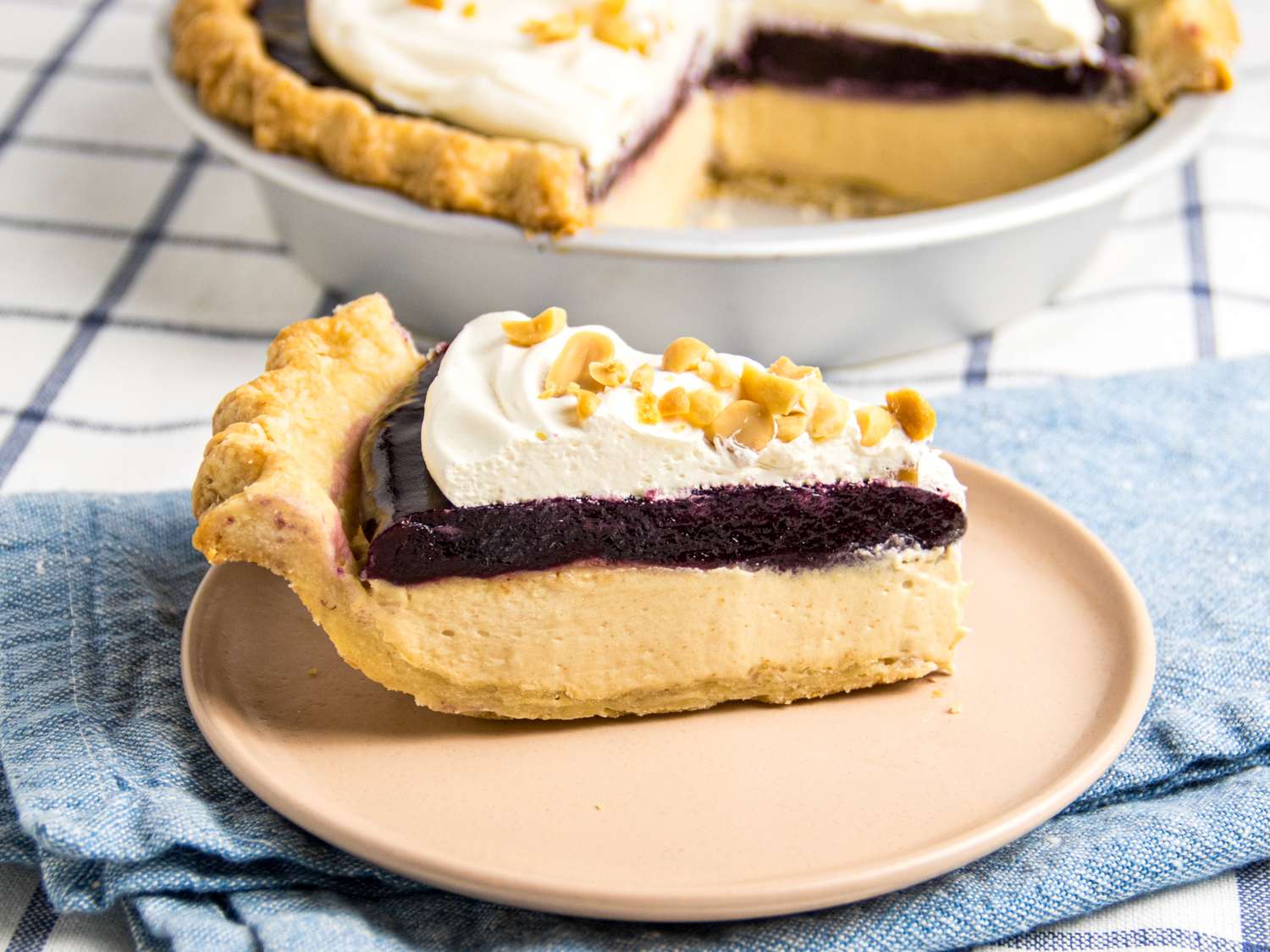 A peanut butter and jelly pie slice on a plate topped with whipped cream and chopped nuts