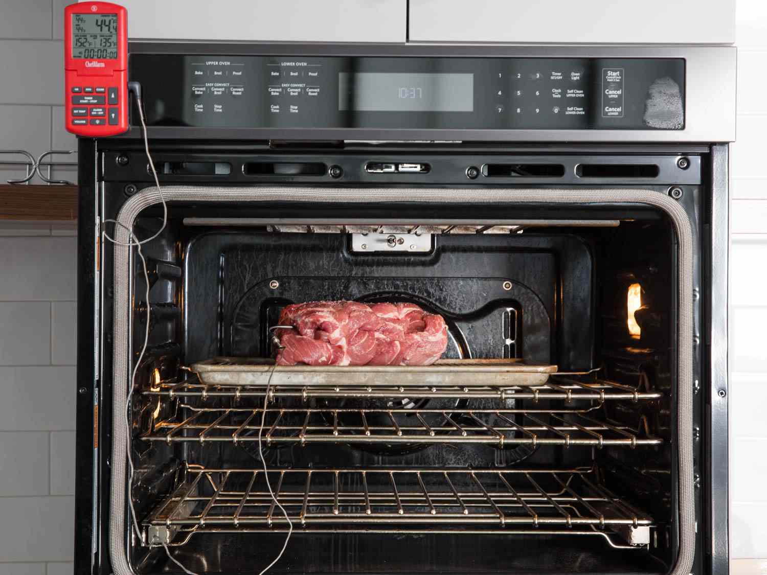 An oven with a probe thermometer displaying temperature attached to meat inside