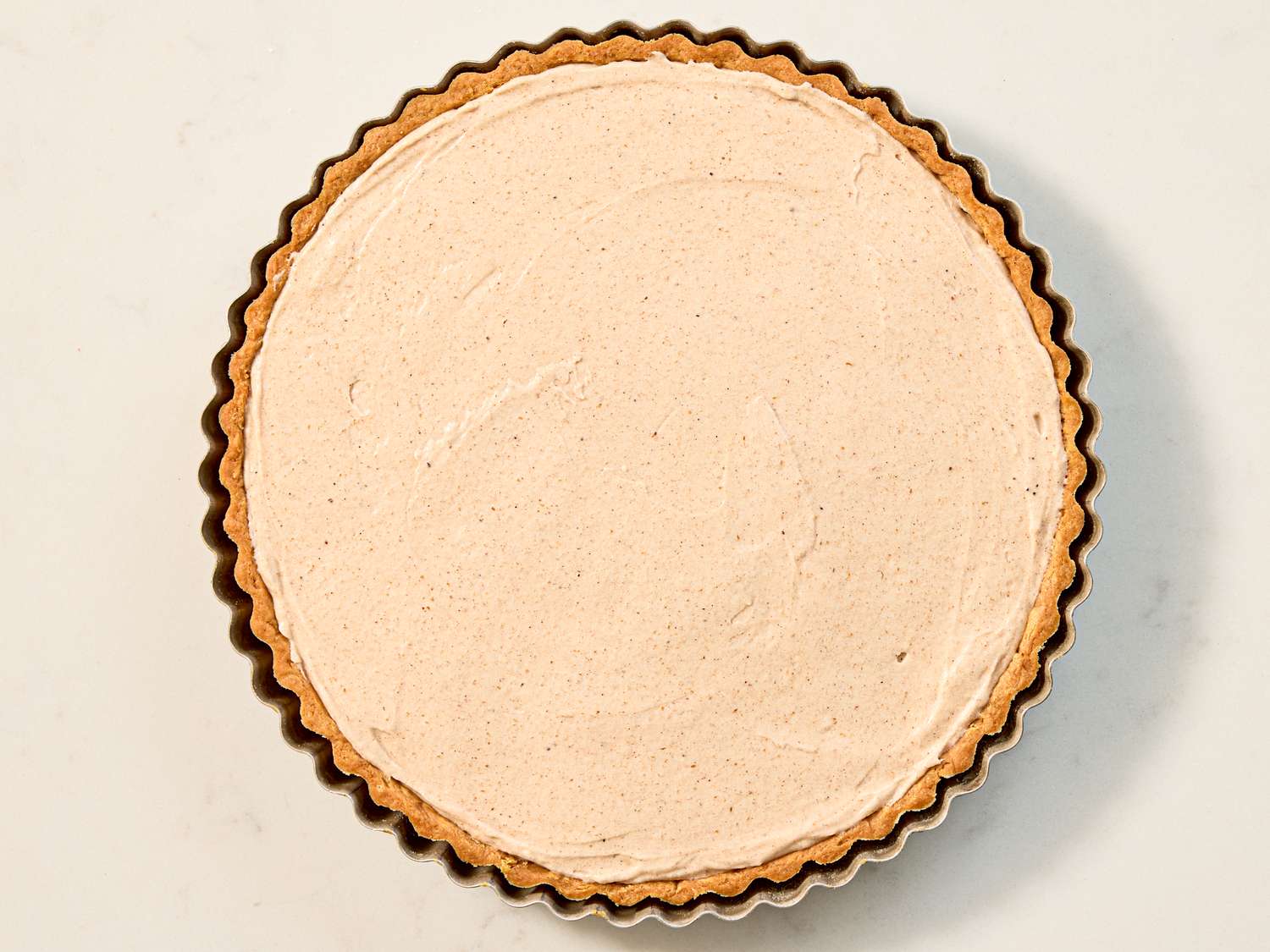 A completed tart with a smooth cream layer in a ridged tart pan viewed from above