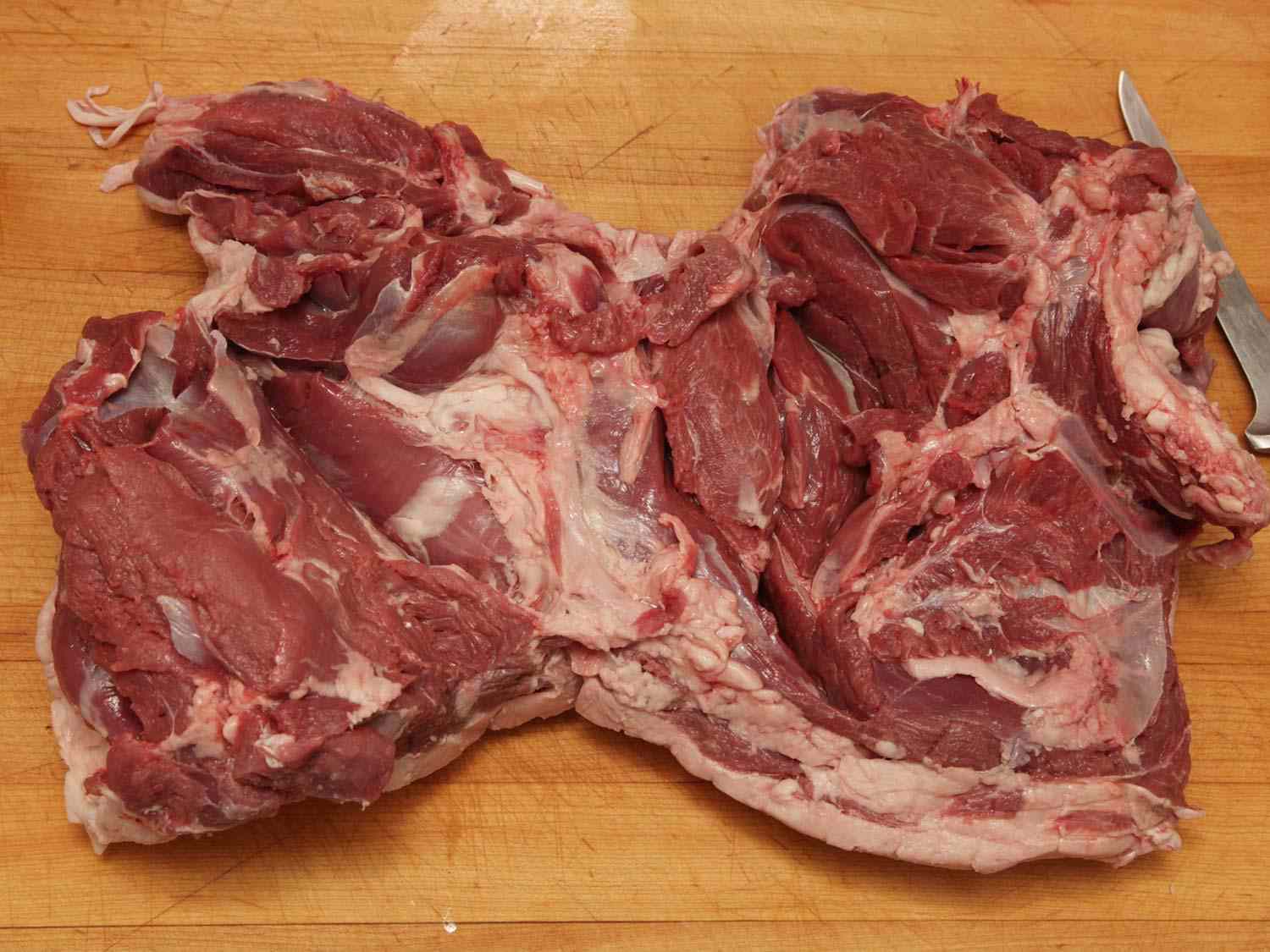 A butterflied leg of lamb, splayed on a cutting board with the interior side facing up.