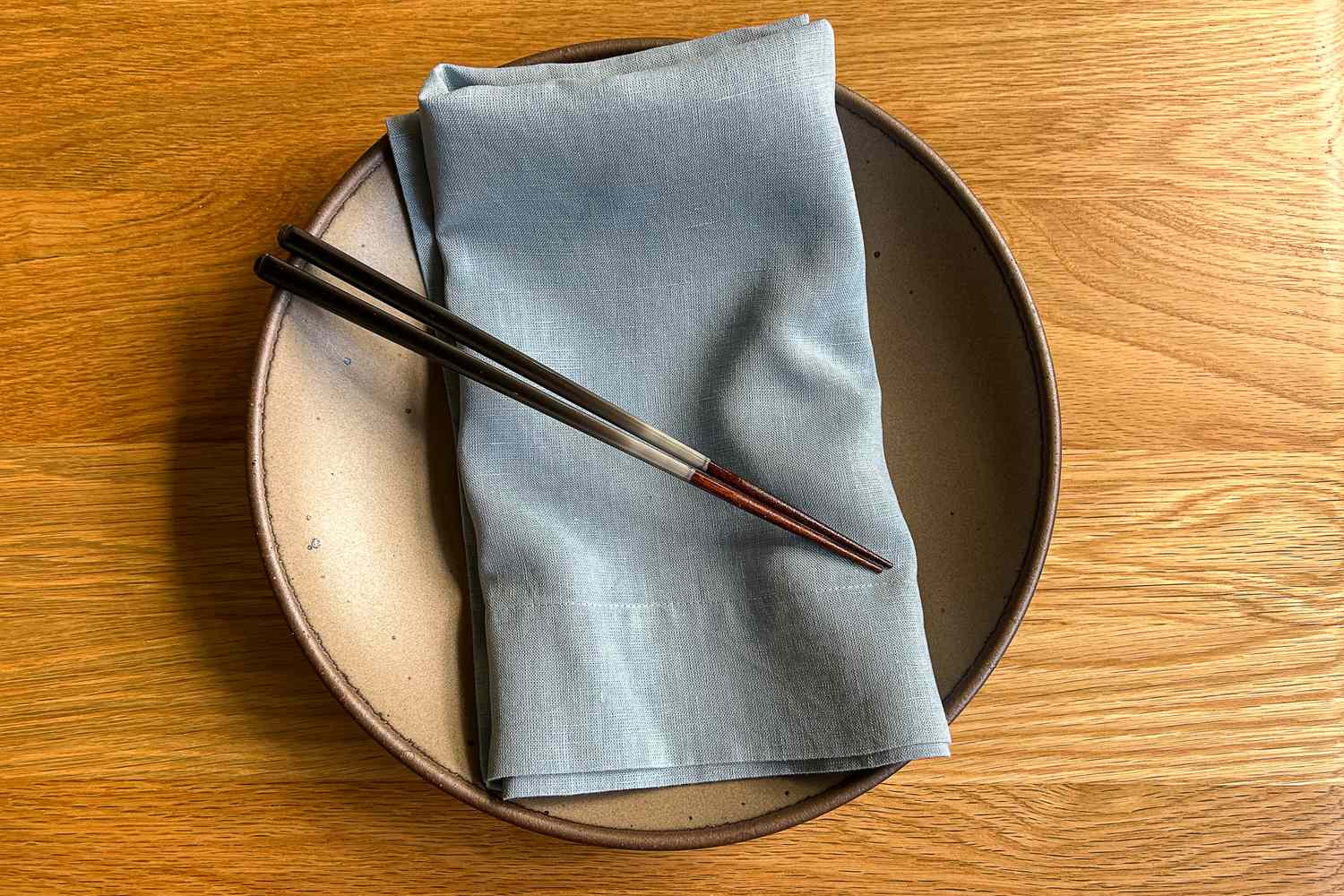 A plate with a folded napkin and a pair of chopsticks resting on it