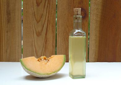 A bottle of homemade melon liqueur set on a table next to a large wedge of cantaloupe.