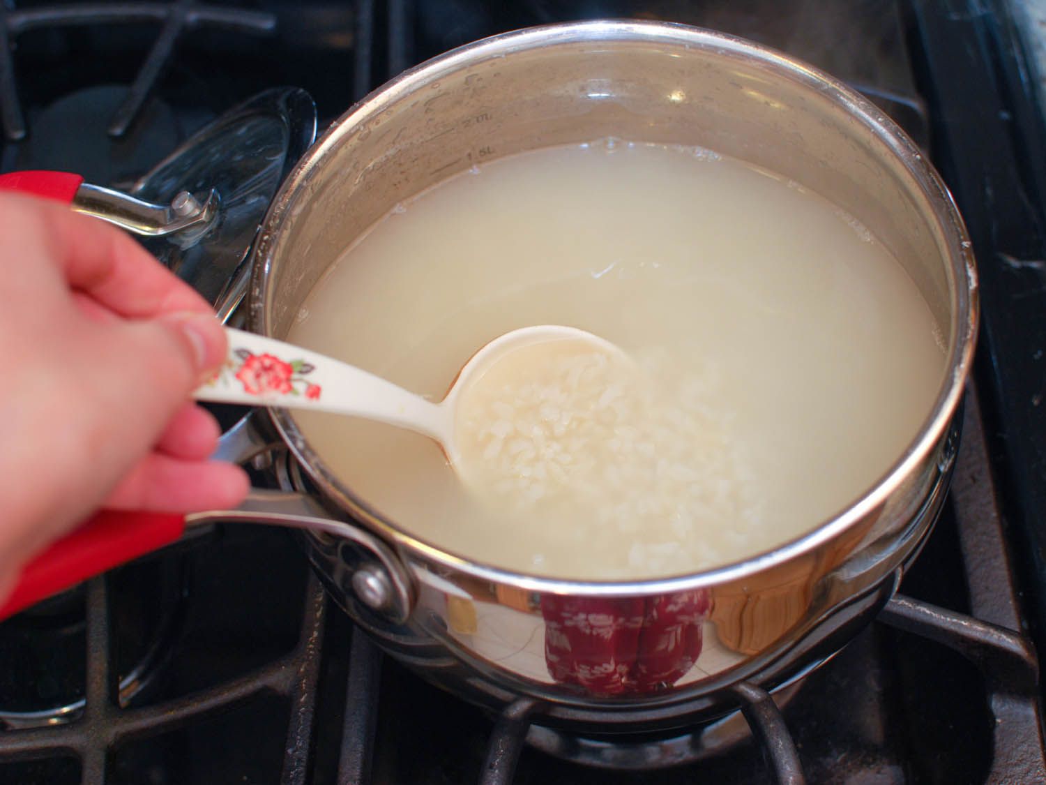 Simmering brown rice is stirred with a spoon.