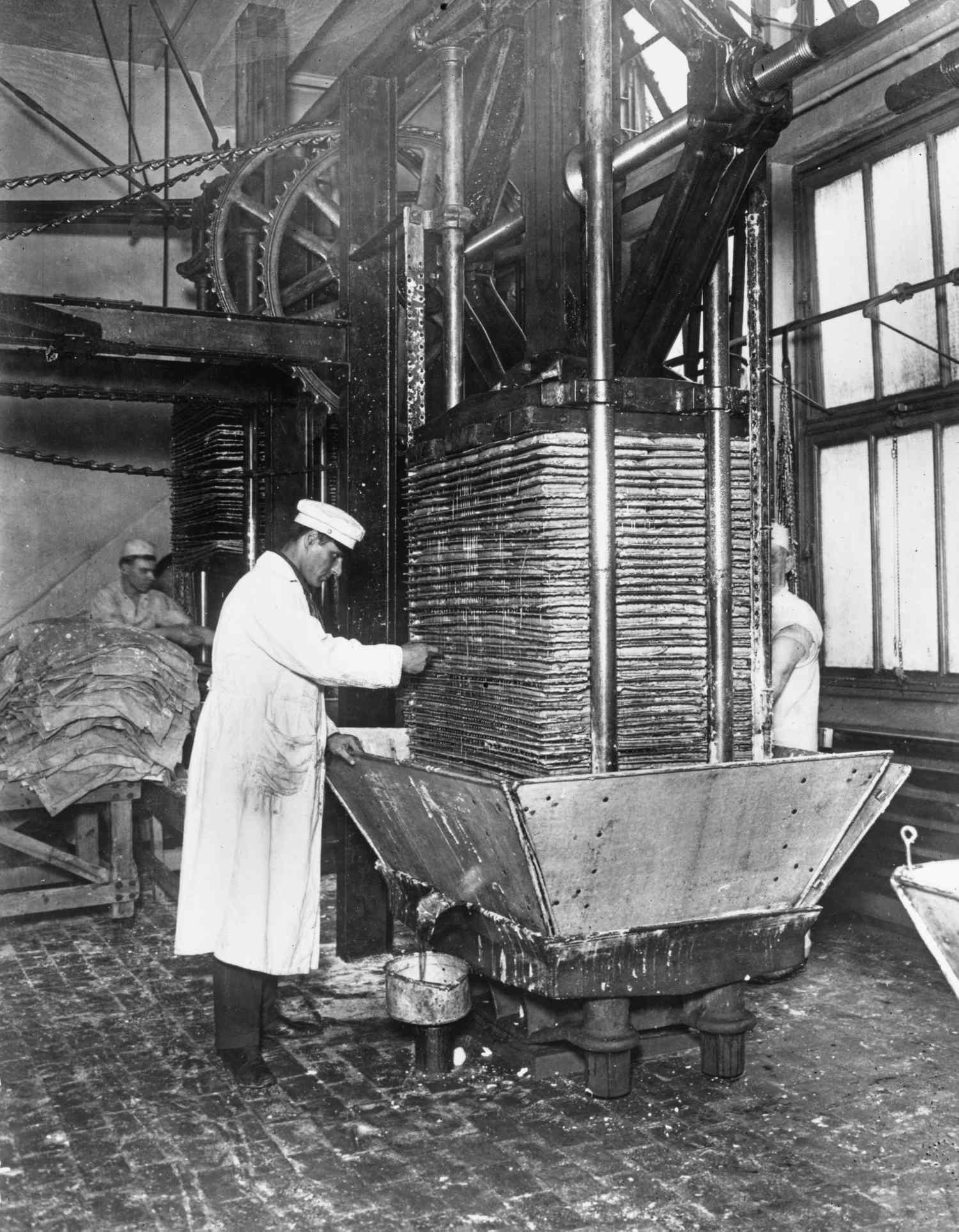 A worker operating an industrial press in a vintage setting likely related to food or drink processing