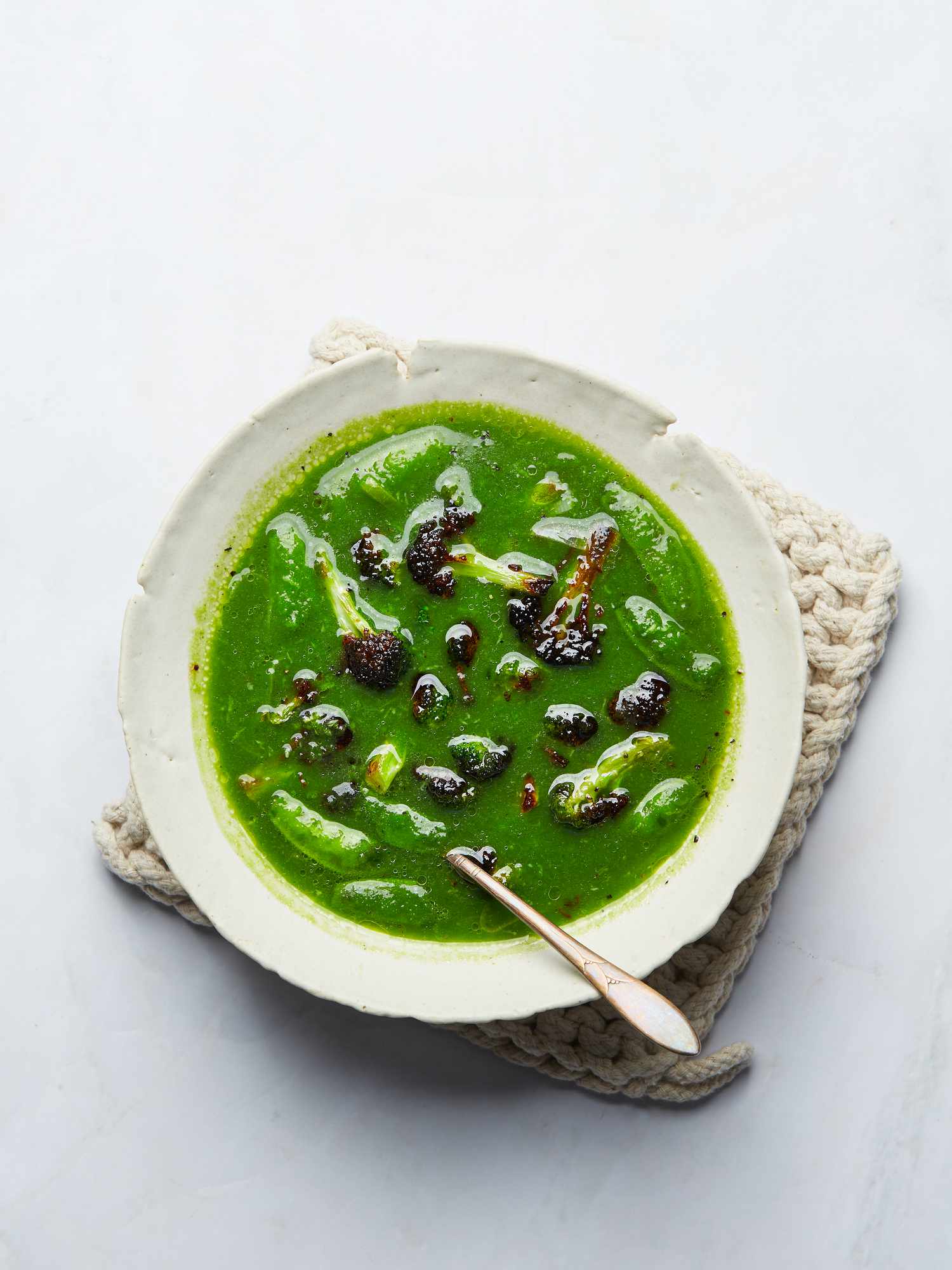 Green Broccoli, leek and snap pea soup from above on a small woven hot pad and spoon in the bowl 