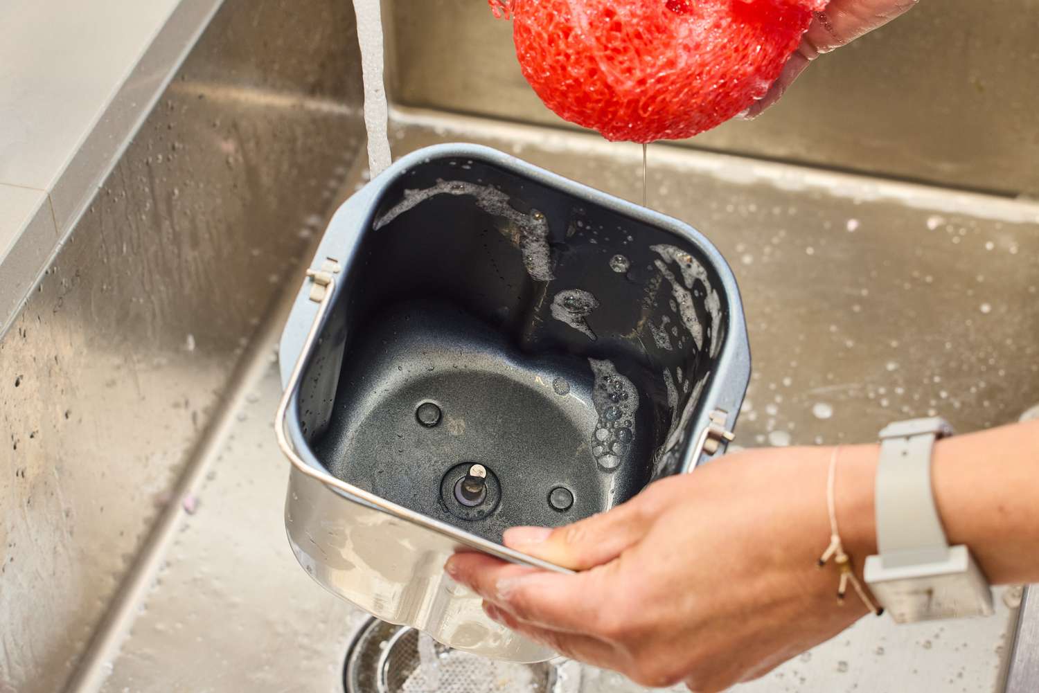 A person washing the basket of the Cuisinart CBK-110 Compact Automatic Bread Maker in a sink