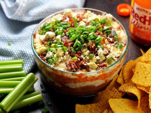 7-layer buffalo chicken dip, served in a glass bowl with tortilla chips and celery sticks.
