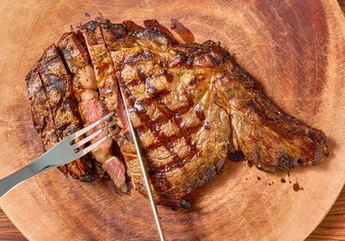 A cooked steak on a wooden board being sliced and held with a fork