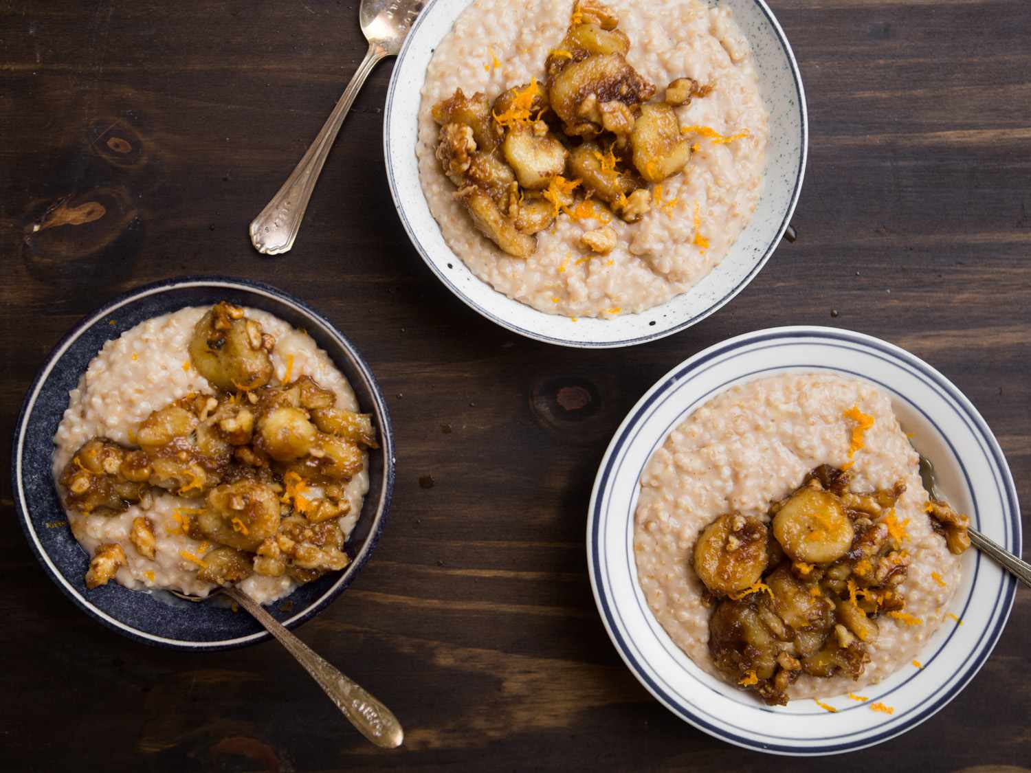 Overhead view of three finished bowls of bananas Foster oatmeal, served on a dark wooden surface.