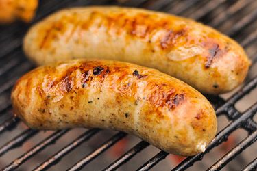 Two links of roasted garlic and feta chicken sausage, browning on the grill.