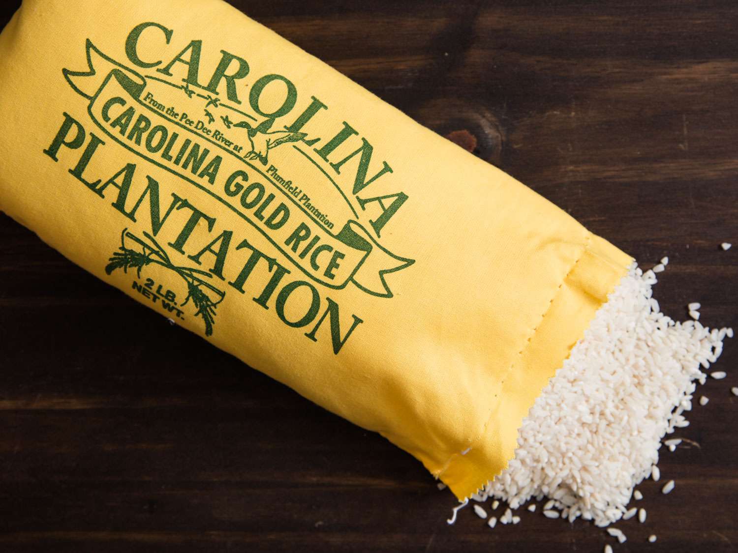 A paper bag of Carolina Gold rice, opened at the bottom with rice spilling out.
