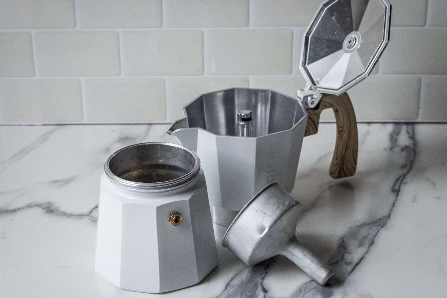 A disassembled stovetop espresso maker on a marble countertop