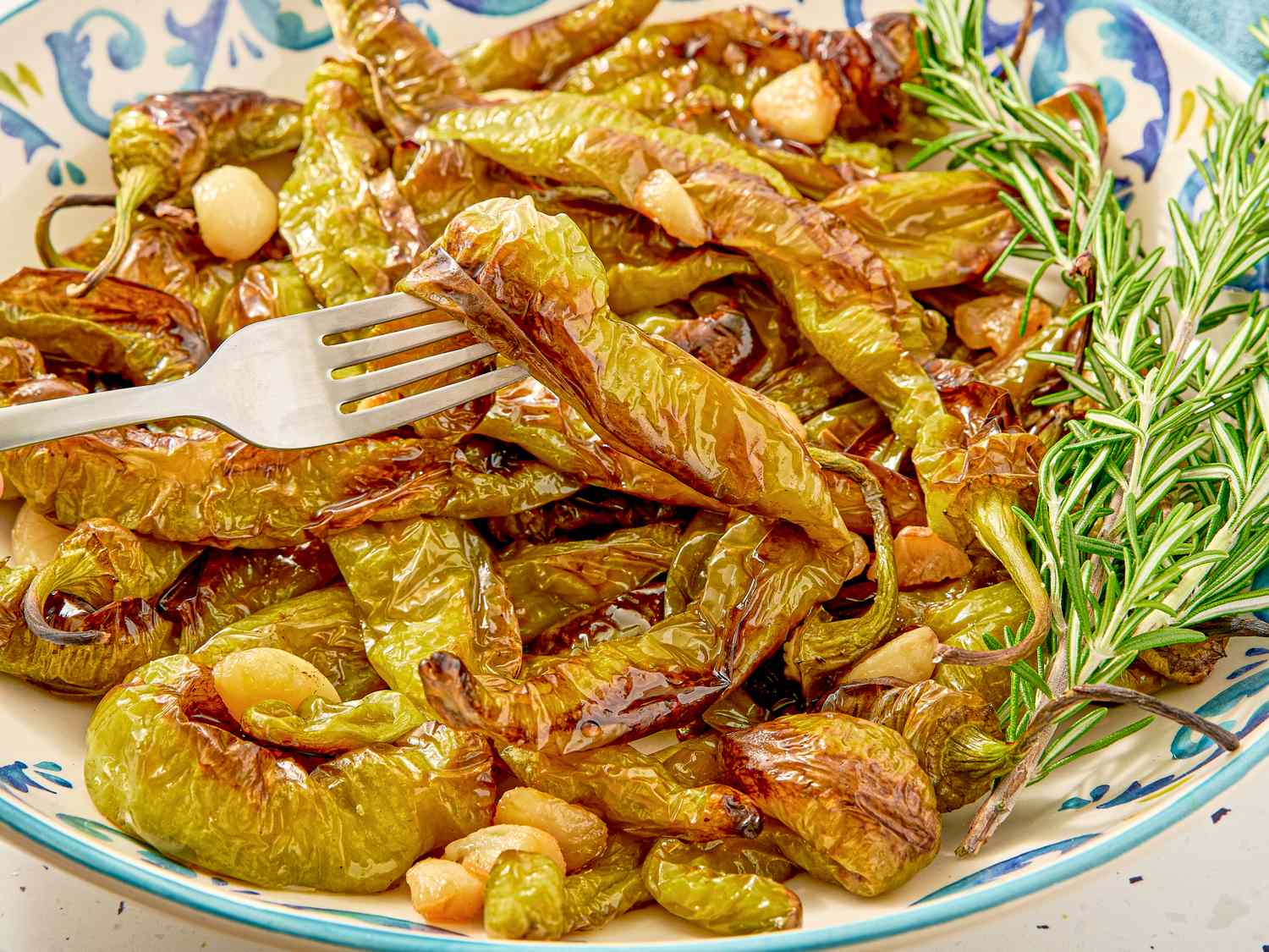 A plate of roasted peppers garnished with garlic and rosemary a fork resting on them