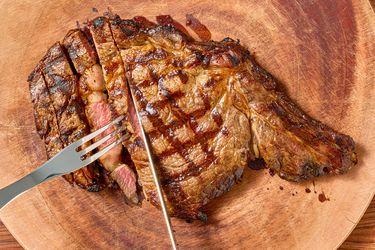 A cooked steak on a wooden board being sliced and held with a fork