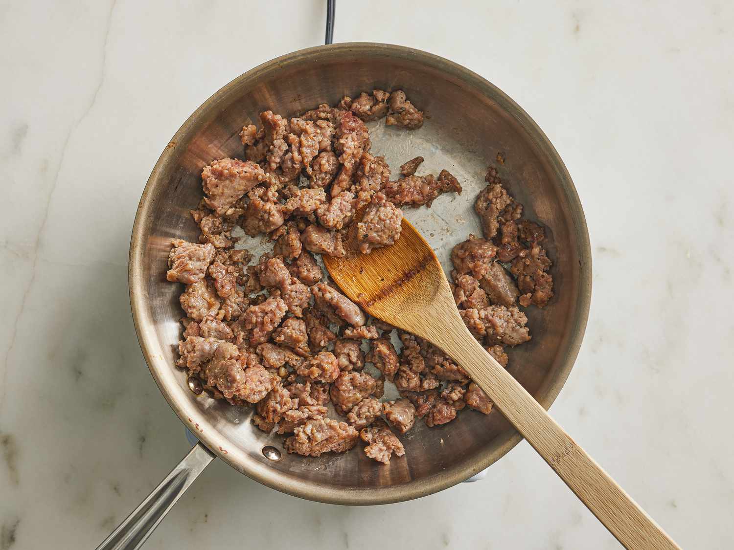 sausage ina skillet being broken up with a wooden spoon