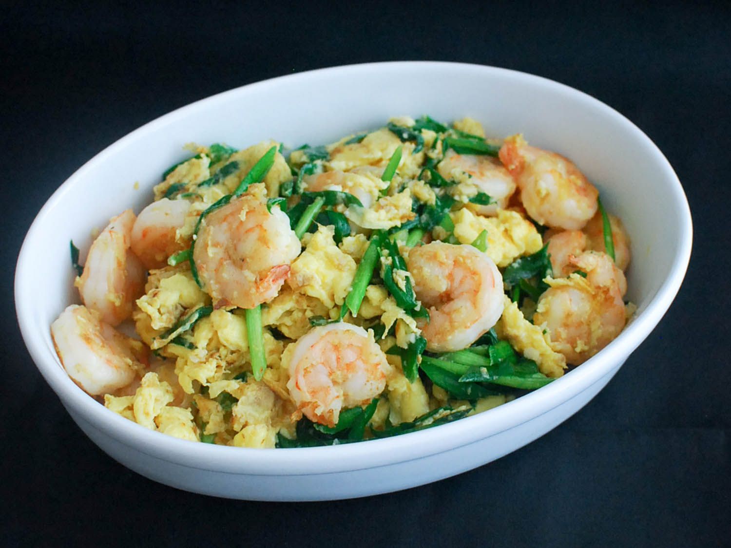 Closeup of a white bowl full of stir-fried shrimp with eggs and Chinese chives.