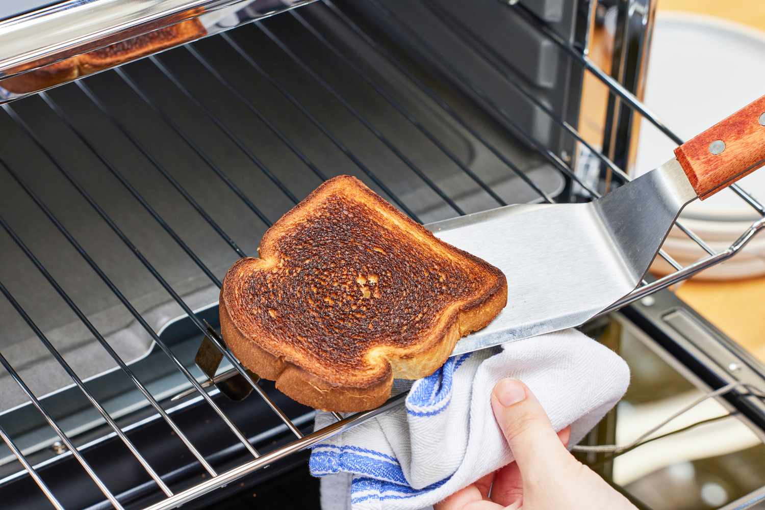 A person removing toasted bread with a towel and spatula from the KitchenAid Dual Convection Countertop Oven with Air Fryer