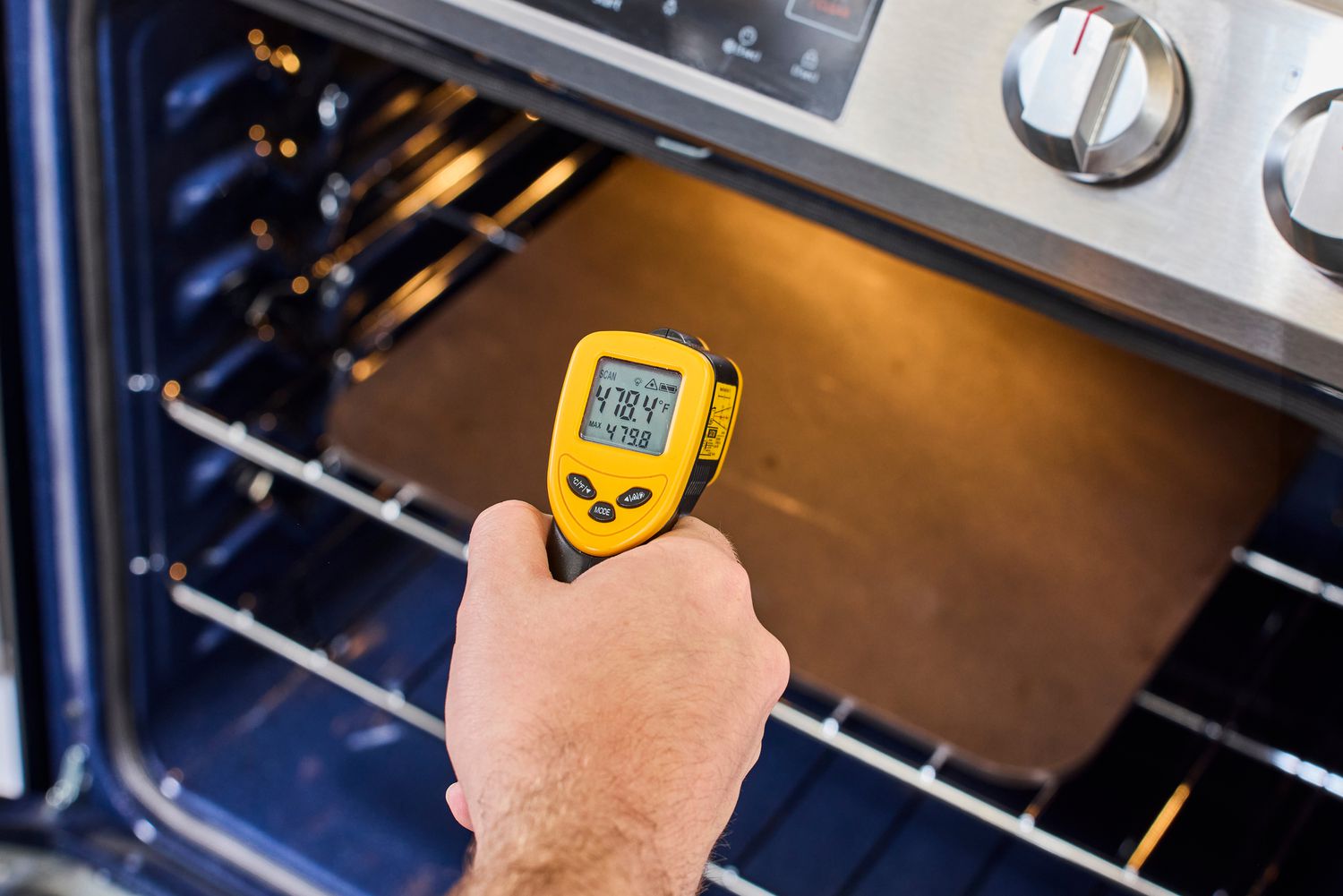 A person taking the temperature of a pizza steel in the oven with an infrared thermometer.