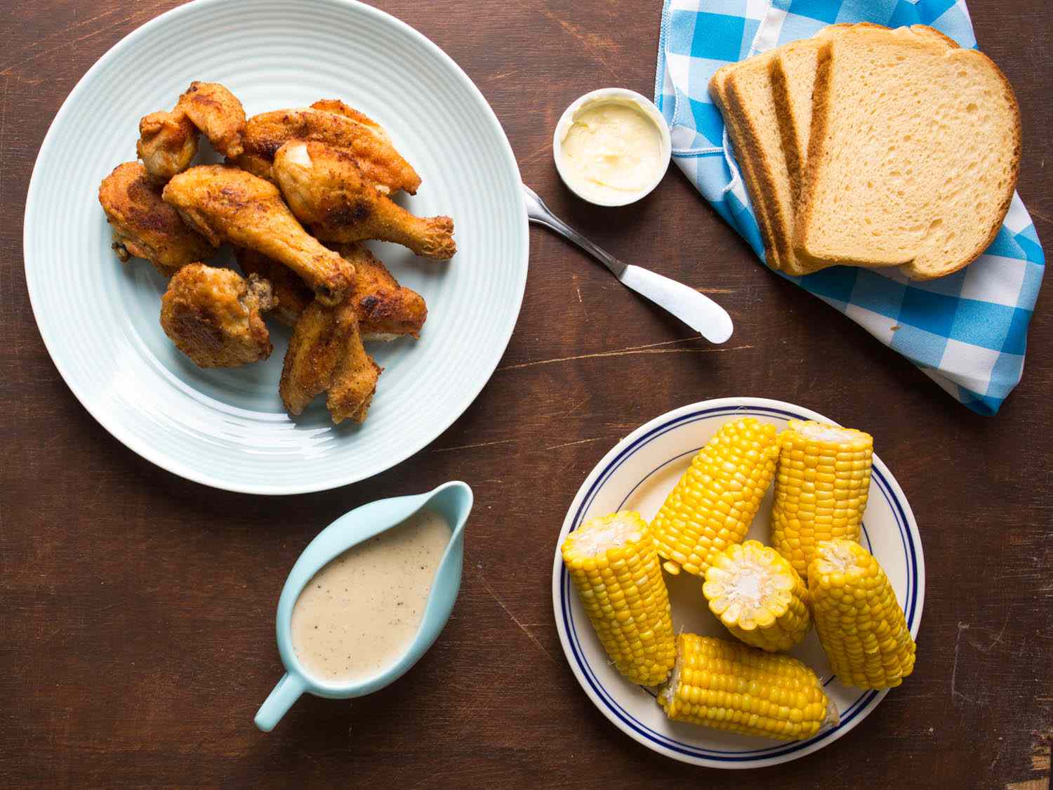 Overhead shot of Maryland fried chicken, white gravy, cobs of corn, and bread.