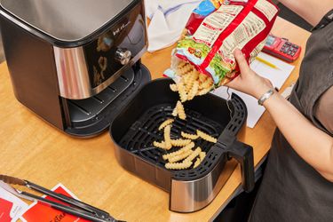 A person emptying a bag of fries into the Instant Vortex Plus 6QT XL Air Fryer basket