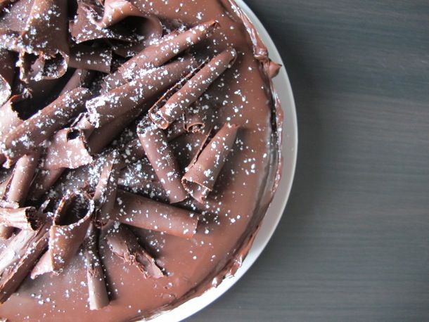 Close-up overhead view of a chocolate mousse cake, decorated with chocolate curls and dusted with confectioner's sugar.