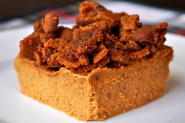 Closeup of a slice of pumpkin custard with cookie crumble topping, served on a white plate.
