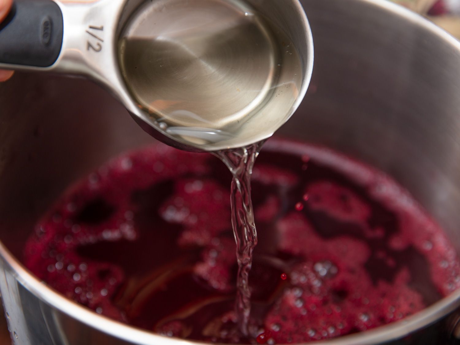 Simple syrup in a 1/2 measuring cup being poured into the strained sorrel mixture.