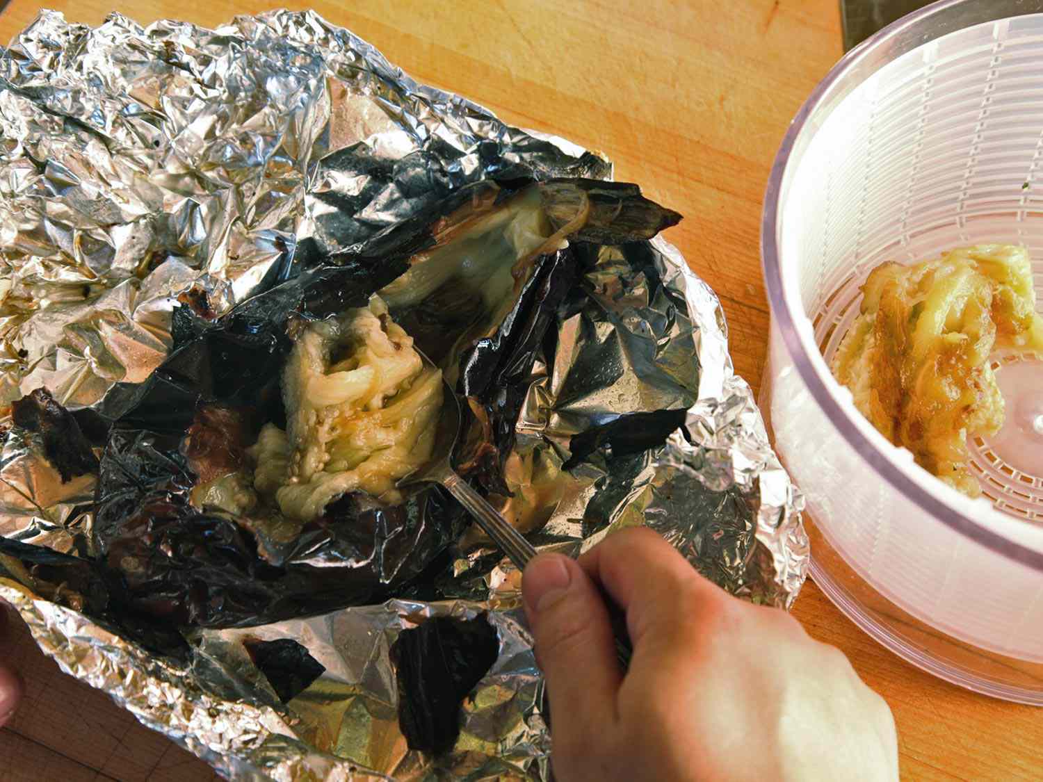 Removing the flesh of roasted eggplant and transferring it to a salad spinner.