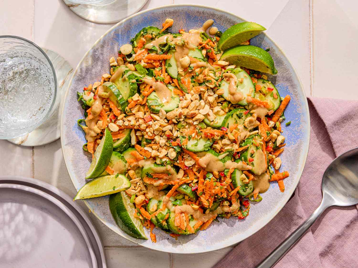 Plate of cucumber salad garnished with crushed peanuts and lime wedges on a table set with dining utensils