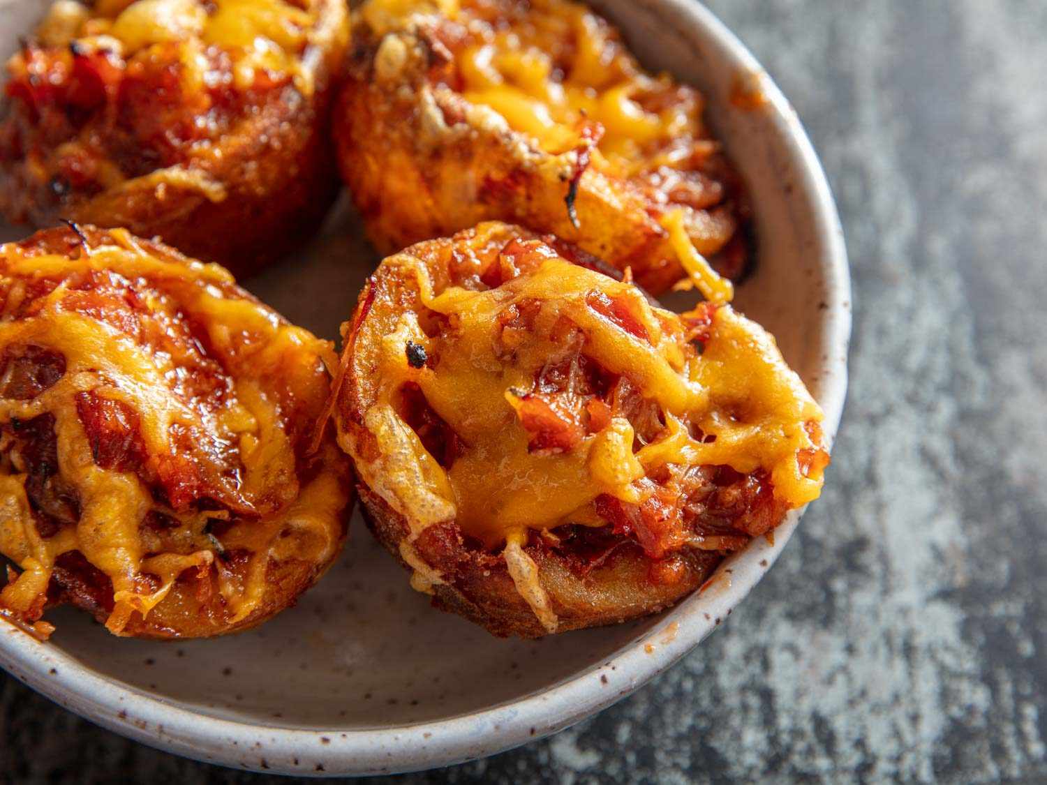 Pulled-pork French-fried potato-skin cups with melted cheddar on top, four pieces in a small bowl.