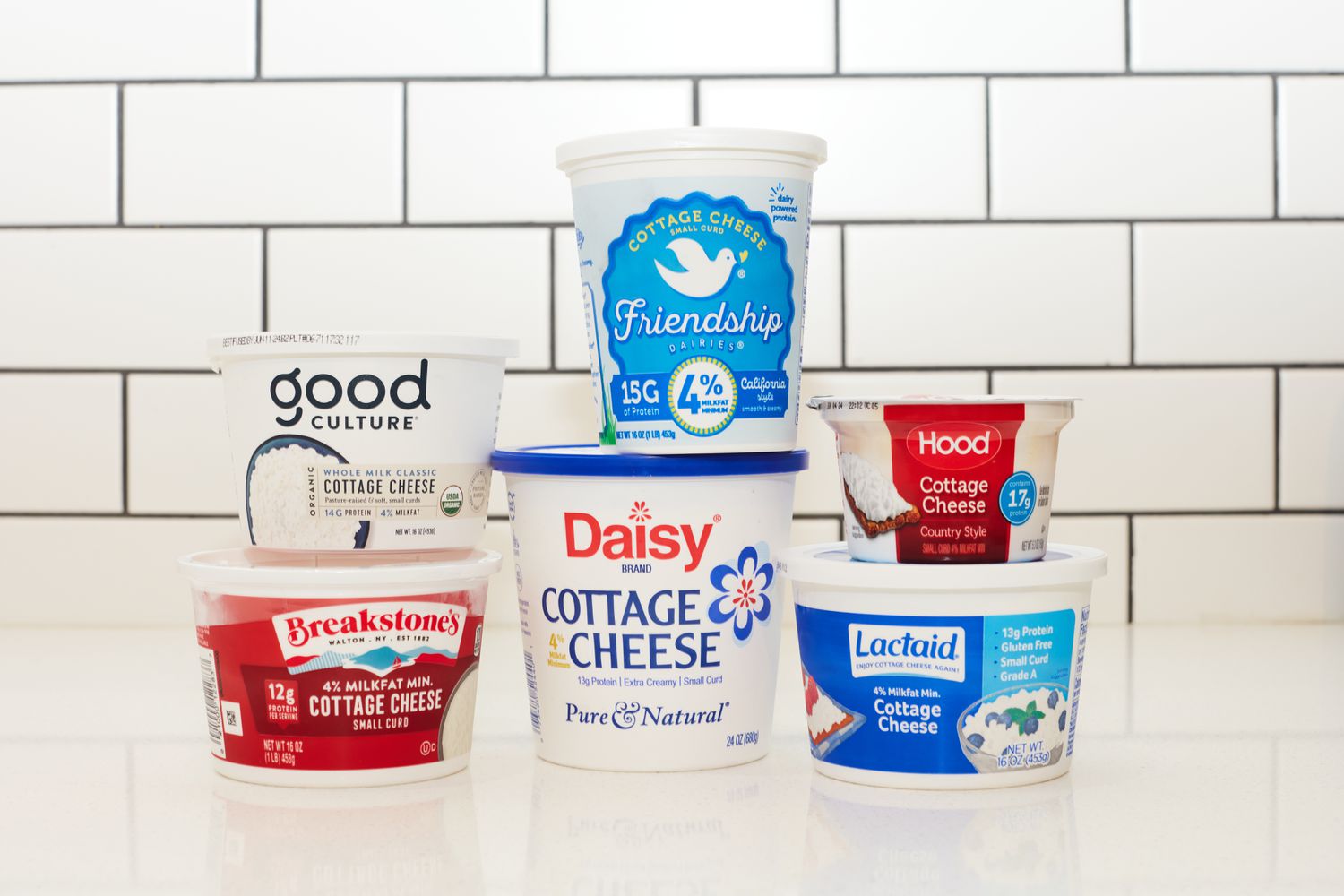 Six brands of cottage cheese stacked atop a counter.