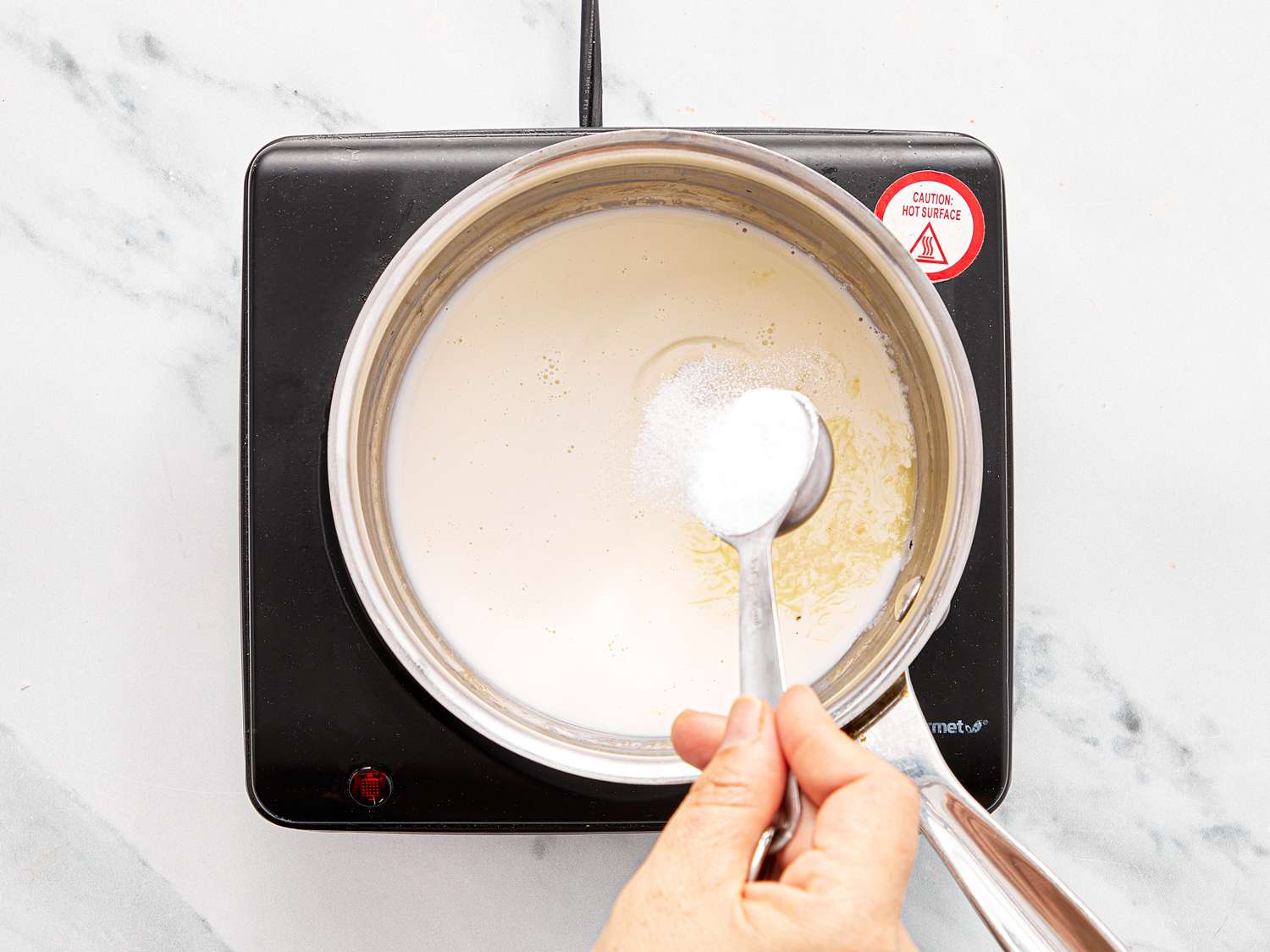 Hands stirring a white liquid in a pan on an induction cooktop