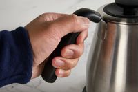 A person gripping the handle of the OXO gooseneck kettle.
