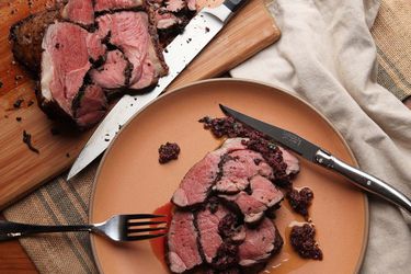 Overhead view of a plate of sliced sous vide leg of lamb with black olives. A cutting board with more sliced lamb is nearby.