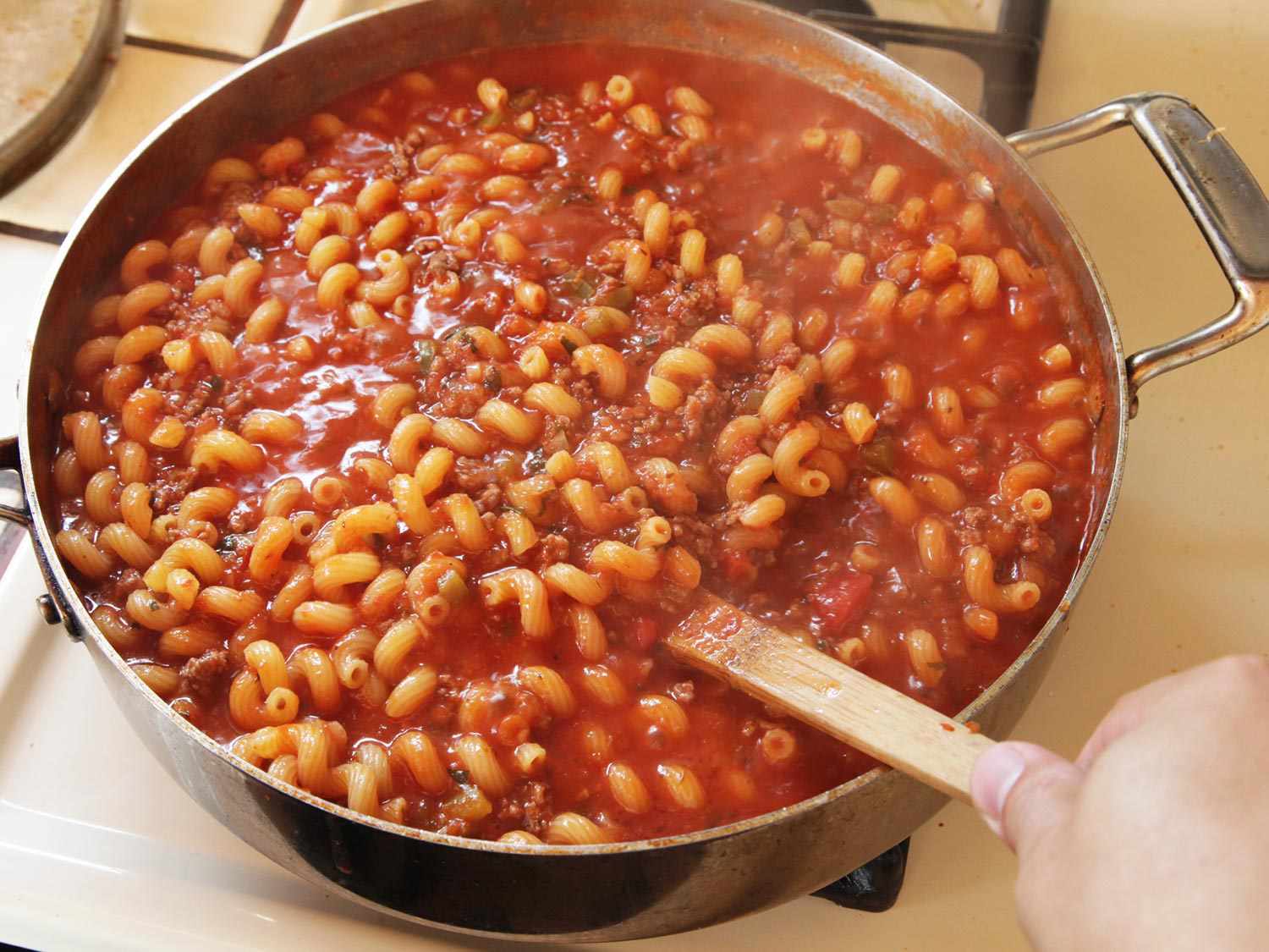 Author stirring the ingredients together so that the pasta is coated and evenly distributed.