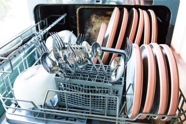 A countertop dishwasher filled with dishes and silverware.